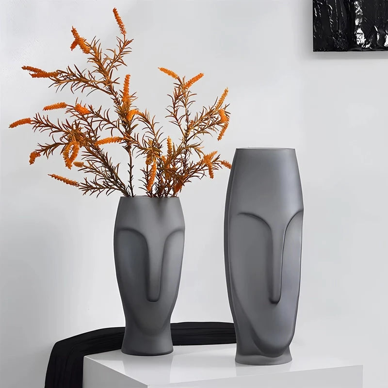 Deux grands vases visage posés sur une table blanche avec des fleurs.
