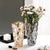 Deux vases en cristal avec fleurs posés sur une table blanche.