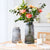 Présentation de deux vases décoratifs gris transparents avec bouquet de fleurs roses