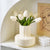 Vase beige sur un meuble blanc avec bouquet de fleurs blanches.