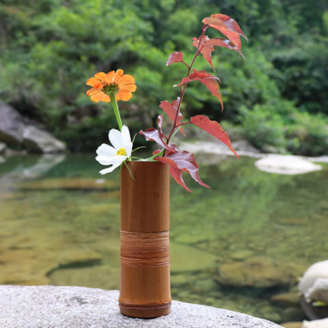 Vase soliflore tubulaire marron en Bambou, présentation en extérieur avec fleurs.