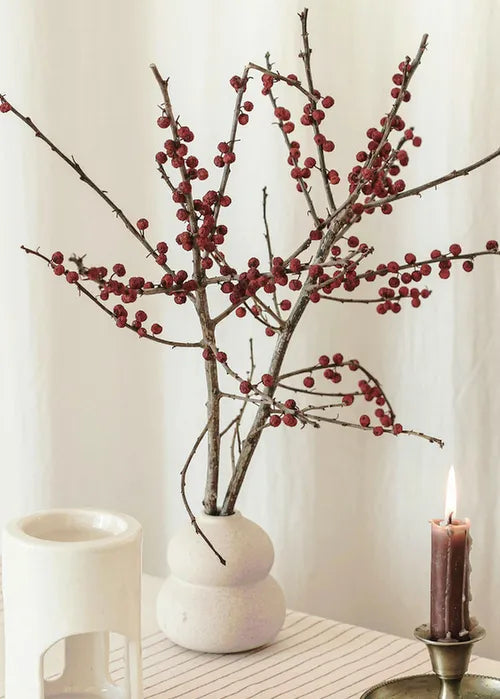 Présentation et mise en scène d'un vase blanc en céramique avec branches séchées et ornement de décoration.