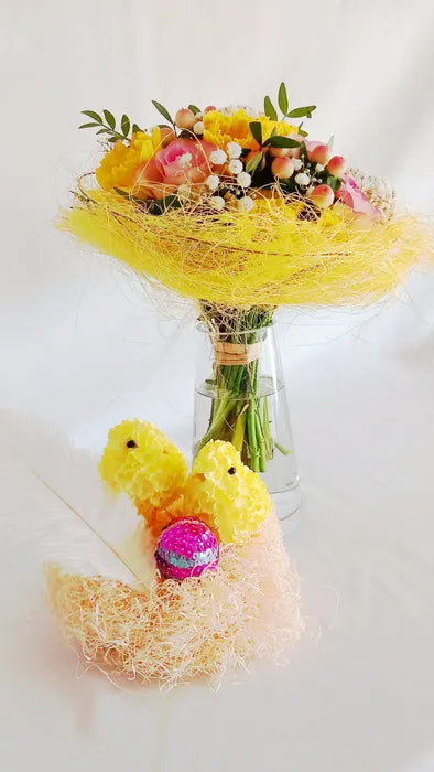 Présentation d'un vase en verre transparent avec un de bouquet de fleurs et ornements de Pâques.