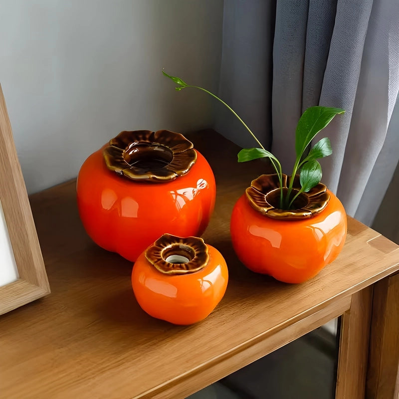 Soliflore Forme Kaki Fruit Exotique en Céramique présentation sur une table en bois de tous les modèles, le modèle M orné d'une plante verte.