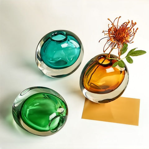 Soliflore rond transparent et coloré en verre, présentation des modèles Bleu, Ambre avec fleur et Vert sur table.
