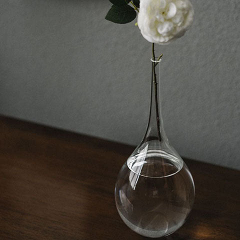 Soliflore style japonais transparent présentation aves rose blanche sur un meuble en bois.