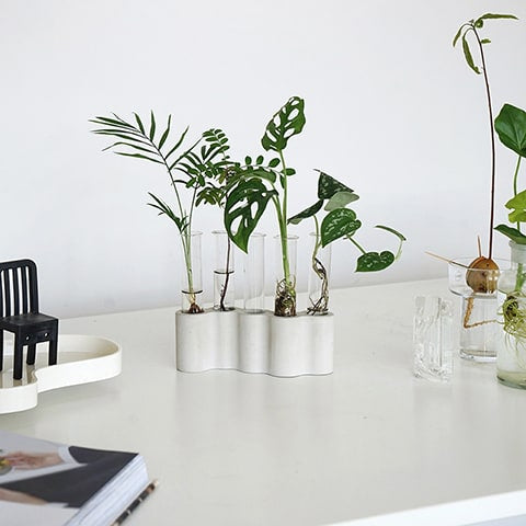 Soliflore tubes ikebana mise en scène avec des plantes et des ornements sur un meuble blanc.