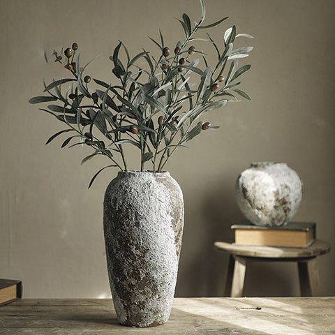 Vase ancien en grès artisanal présentation modèle grand avec branches d'olivier, modèle petit en arrière plan posé sur un tabouret en bois.