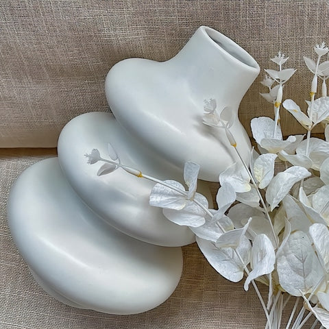 Vase Blanc Design Anneaux Superposés en céramique présentation couché sur un canapé avec fleurs blanches à côté.