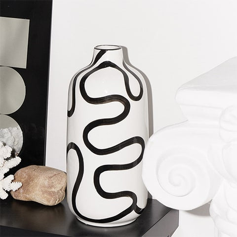 Vase blanc lignes abstraites noires design présentation sur table sans fleurs avec ornements disposés autour.
