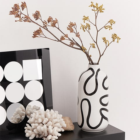 Vase blanc lignes abstraites noires design présentation sur table avec fleurs et ornements.