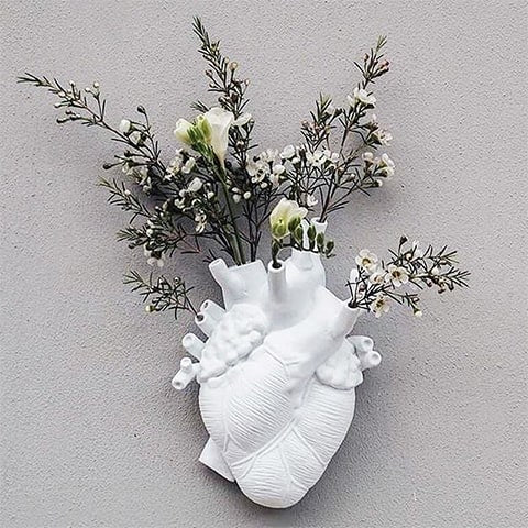 Vase Cœur Humain Blanc en céramique présentation du modèle Grand accroché sur un mur avec des fleurs blanches.
