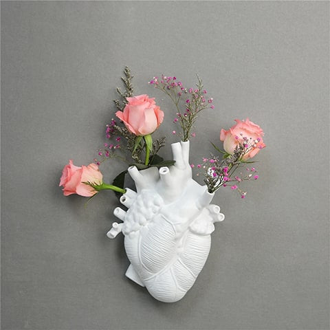 Vase cœur humain blanc accroché sur un mur gris avec des roses.