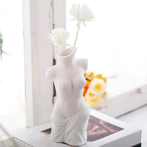 Vase Corps Femme en Céramique présentation posé sur un livre avec des fleurs blanches.