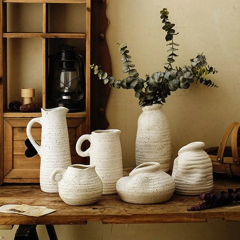 Vase cruche vintage blanc moucheté en céramique, présentation tous les modèles avec des branches d'eucalyptus sur une table en bois dans un salon.
