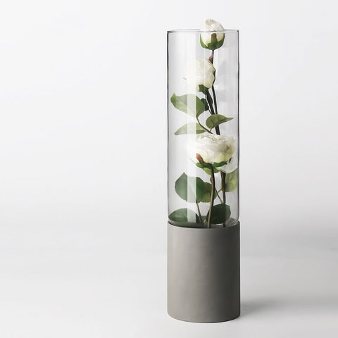 Vase cylindrique bi-matière transparent et gris, en verre et céramique, présentation du modèle A avec roses blanches.