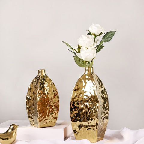 Vase doré relief asymétrique en céramique présentation des modèles S vide et L avec fleurs blanches sur un table avec ornements.