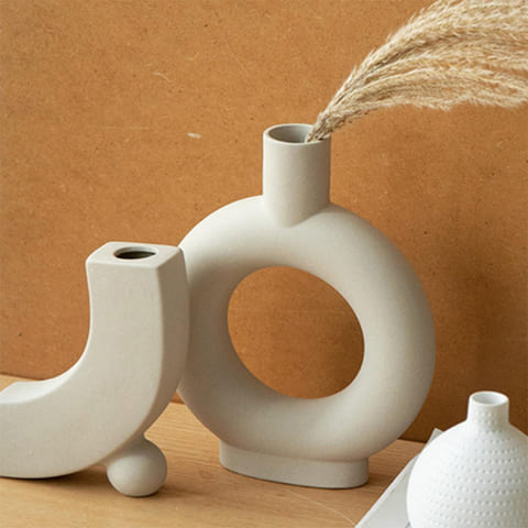Vase Design Forme Donut en céramique présentation avec fleurs séchées sur une table en bois avec ornements.