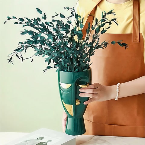 Vase en Forme de Visage Style Nordique en céramique présentation du modèle Vert et doré avec feuillage, tenu en main.
