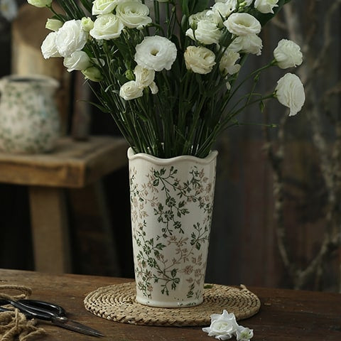 Vase d'époque motif feuillages verts en céramique modèle D avec bouquet de fleurs blanches sur une table  bois ancien.