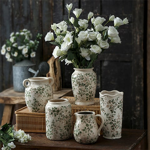 Vase d'époque motif feuillages verts, présentation de tous les modèles sur une table en bois avec bouquet de fleurs blanches.