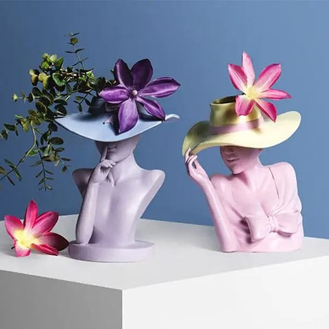 Vase Femme au Chapeau en résine présentation des modèles violet B et Rose A avec fleurs sur un meuble blanc.