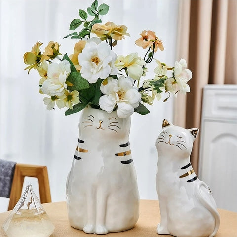 Vase blanc en forme de chat blanc en céramique avec fleurs présentation sur une table avec ornements.