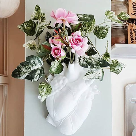 Vase mural cœur humain blanc présentation avec fleurs et tiges de feuilles vertes, accroché au mur.