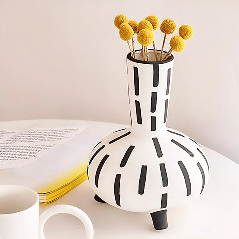 Vase original noir et blanc lignes pointillées en céramique présentation sur une table avec des fleurs jaunes.