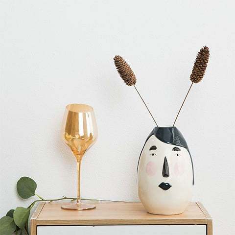 Vase ovale blanc visage original en céramique présentation avec ornements sur un meuble en bois.