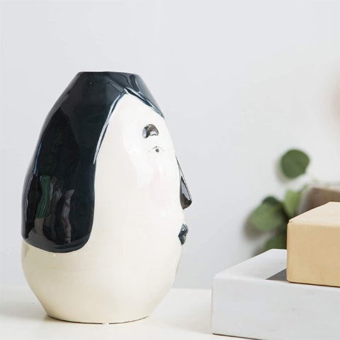 Vase ovale blanc visage original en céramique présentation de profil sans fleurs sur une table blanche.