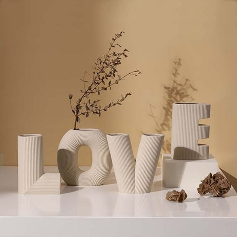 Vase rayé Art créatif lettres Love présentation, modèle blanc avec tiges dans la lettre O, mise en scène lettre E sur un socle, lettres L et V posés sur un meuble blanc brillant.