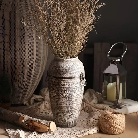 Vase Rétro Cerclage Cuivré avec Poignées Têtes de Lion en céramique, présentation modèle L avec fleurs séchées sur une table avec ornements décoratifs anciens.