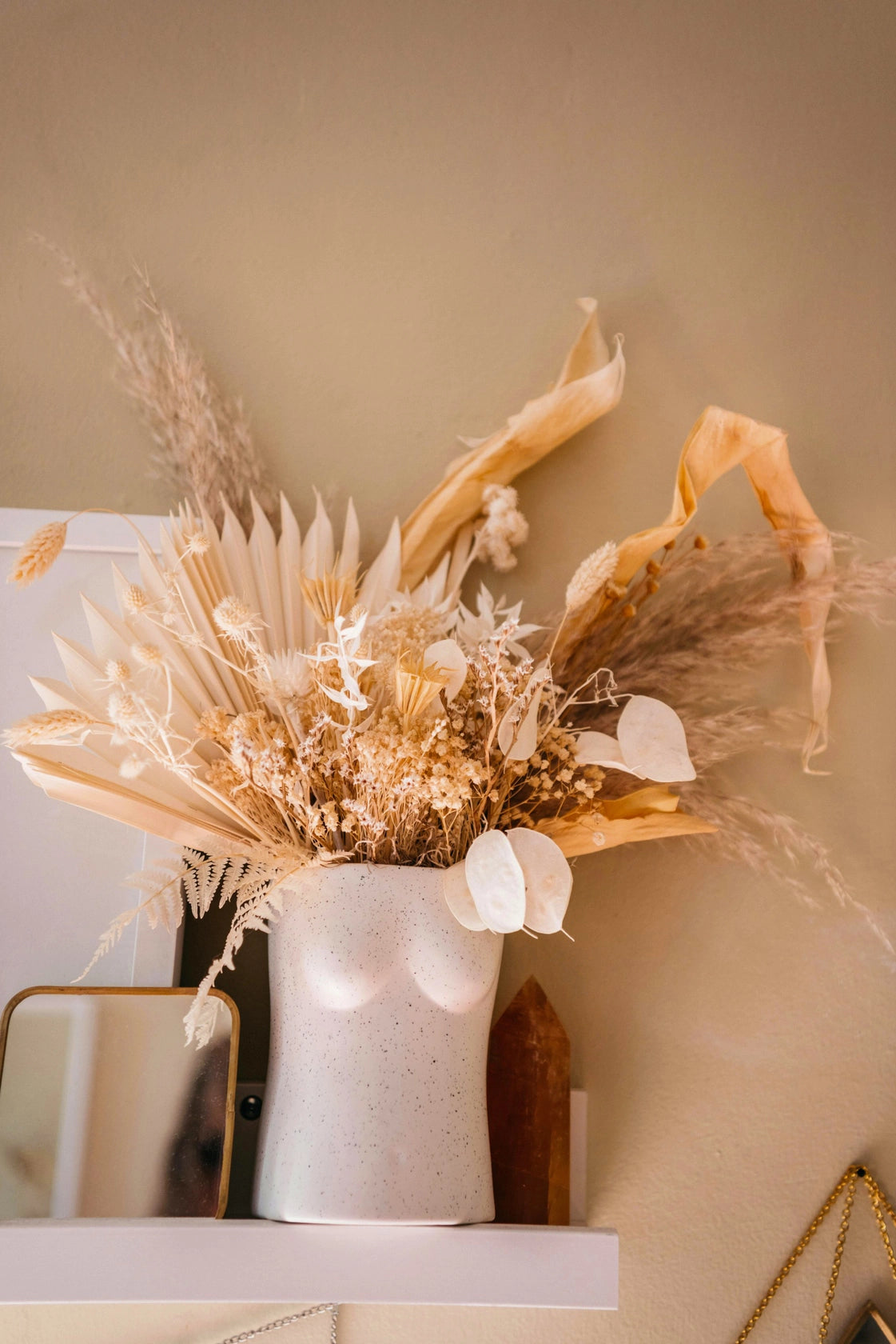 vase seins blanc en céramique avec bouquet de fleurs séchées sur une étagère
