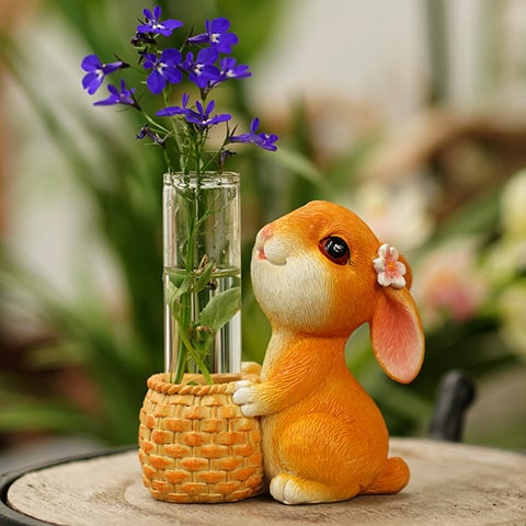 Vase soliflore lapin joyeux en verre et résine, présentation avec fleurs violettes sur une table.