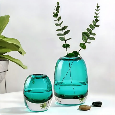 Vase soliflore ovale bleu translucide en verre présentation des modèles Bleu S et M avec plantes sur une table.