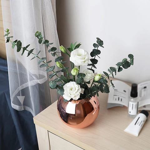 Vase Sphérique Moderne Design Raffiné en métal, modèle rose gold sur un chevet avec bouquet de fleurs.