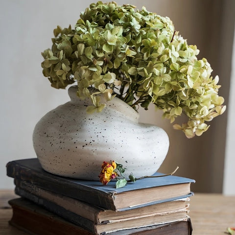 Vase Vintage Blanc Moucheté en céramique, présentation du modèle C avec fleurs, posé sur des livres sur une table en bois.