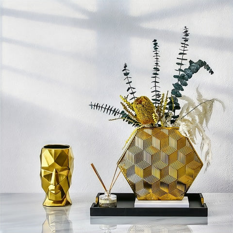 Vase visage design doré en céramique présentation sans fleurs sur une table blanche avec ornements dorés.