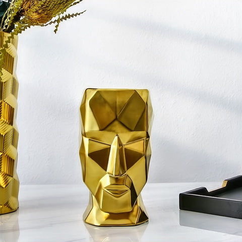 Vase visage design doré en céramique présentation posé sur une table blanche.