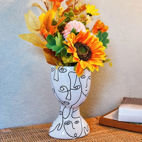 Vase visages abstraits original en céramique présentation avec bouquet de fleurs sur une table.
