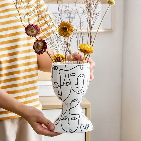 Vase visages abstraits original en céramique tenu en main orné de fleurs séchées.