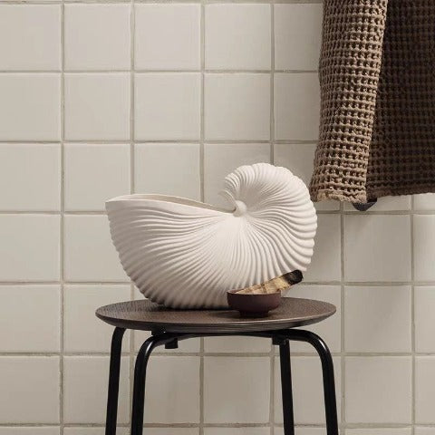 Présentation du vase coquillage blanc sans fleurs sur un tabouret dans une salle de bain.