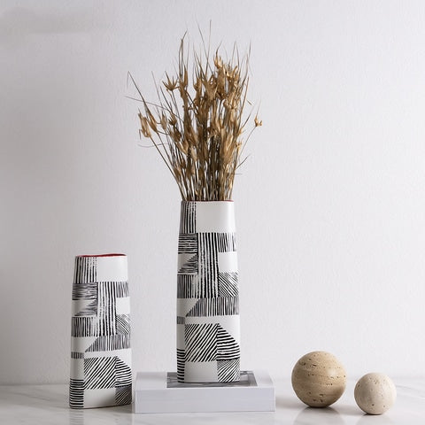 Vase Rectangulaire lignes noires sur fond blanc, présentation avec décorations, tiges de fleurs séchées et un livre.