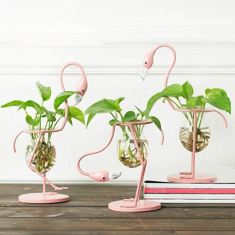 Vase Soliflore Flamant Rose en Verre et fer, Styles A, B et C, présentation avec plantes vertes sur un meuble en bois.