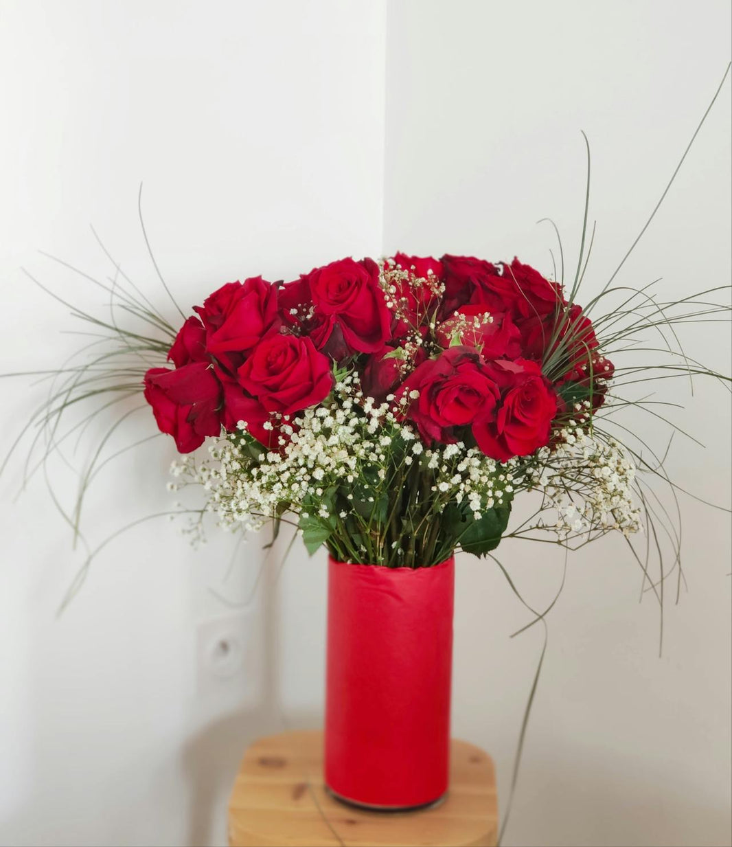 Vase entourer de papier cadeau rouge avec un bouquet de fleurs rouge