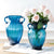 Deux vases bleus avec anse et bouquet de fleurs posés sur une table.
