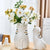 Deux vases en forme de chat blanc avec bouquet de fleurs posé sur une table en bois.
