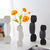 Plusieurs Soliflores Design Minimaliste Forme Géométrique présentation avec fleurs sur une table blanche.