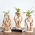 Plusieurs soliflores en bois avec plantes vertes posés sur une table en bois.